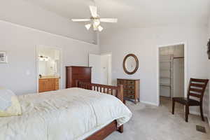 Owners suite with light colored carpet, a walk in closet, vaulted ceiling, ceiling fan, and connected bathroom