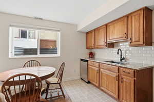 Kitchen with light stone countertops, brown cabinets, decorative backsplash, and dishwasher