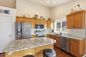Kitchen with appliances with stainless steel finishes, light stone countertops, a kitchen breakfast bar, a kitchen island, and dark wood-style floors
