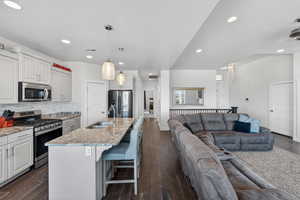 Kitchen with stainless steel appliances, a breakfast bar area, open floor plan, dark wood-style flooring, and a kitchen island with sink