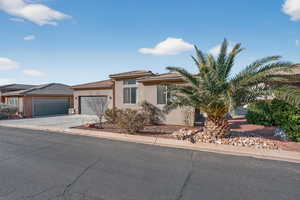 View of front facade featuring stucco siding, a garage, concrete driveway, a tiled roof, and solar panels