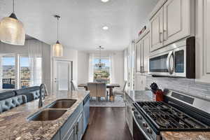 Kitchen with dark stone counters, stainless steel appliances, pendant lighting, dark wood-style floors, and a textured ceiling