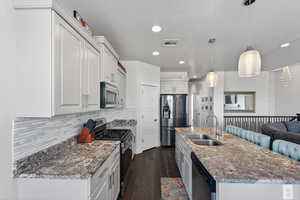 Kitchen with stainless steel appliances, dark wood-style flooring, light stone counters, hanging light fixtures, and white cabinets