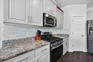 Kitchen featuring appliances with stainless steel finishes, light stone counters, dark wood-style flooring, and white cabinets