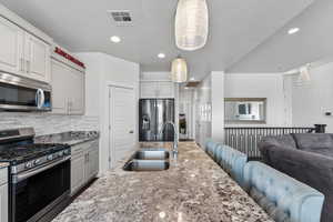 Kitchen featuring appliances with stainless steel finishes, light stone counters, open floor plan, recessed lighting, and pendant lighting
