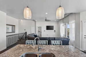 Kitchen featuring a ceiling fan, hanging light fixtures, a textured ceiling, open floor plan, and light stone countertops