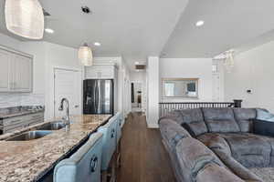 Kitchen with light stone counters, stainless steel refrigerator with ice dispenser, dark wood-type flooring, hanging light fixtures, and open floor plan