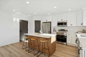 Kitchen with appliances with stainless steel finishes, recessed lighting, white cabinets, a kitchen bar, and a center island
