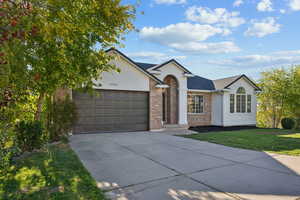 Ranch-style house with stucco siding, concrete driveway, brick siding, a front lawn, and a garage