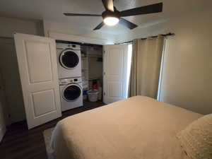 Bedroom with stacked washer / drying machine, dark wood finished floors, ceiling fan, and a closet