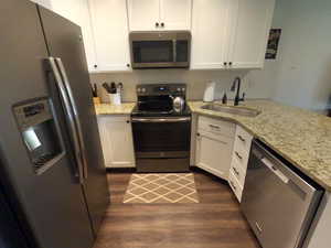 Kitchen with stainless steel appliances, white cabinets, light stone countertops, and decorative backsplash