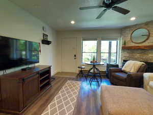 Living room with dark wood-type flooring, a ceiling fan, a stone fireplace, and recessed lighting