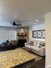 Living room featuring a textured ceiling, a fireplace, dark wood finished floors, ceiling fan, and recessed lighting