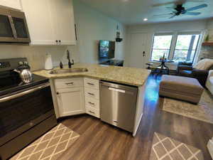Kitchen featuring stainless steel appliances, a peninsula, white cabinets, dark wood-type flooring, and open floor plan