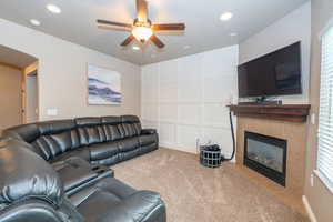 Living room with a tiled fireplace, light colored carpet, a ceiling fan, and recessed lighting