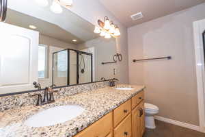 Full bath featuring a shower stall, double vanity, and dark tile patterned flooring