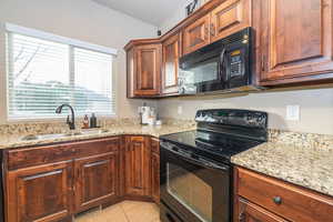Kitchen featuring black appliances, light stone countertops, and light tile patterned floors