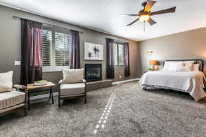 Carpeted bedroom with a glass covered fireplace, ceiling fan, and a textured ceiling