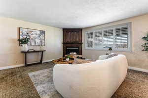 Living room featuring a glass covered gas fireplace, planation shutters, and carpet flooring