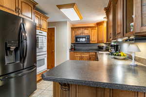 Kitchen with black appliances, brown cabinets, a peninsula, dark countertops, and light tile patterned floors