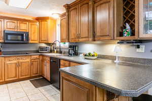 Kitchen featuring brown cabinets, dark countertops, stainless steel microwave, black dishwasher, and a peninsula