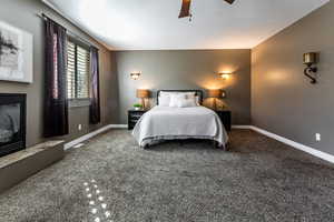 Bedroom with a glass covered fireplace, carpet floors, ceiling fan, and a textured ceiling