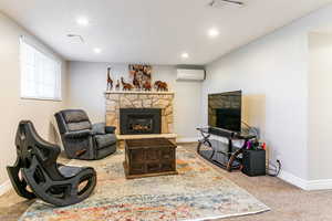 Living room with a stone fireplace, light carpet, recessed lighting, and an AC wall unit