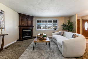 Living room featuring a glass covered gas fireplace, planation shutters, and carpet flooring