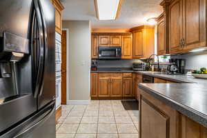 Kitchen with stainless steel refrigerator with ice dispenser, Double wall ovens, cooktop stove, brown cabinets, Corian countertops, light tile patterned flooring.