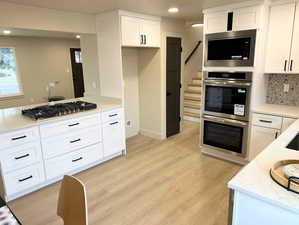 Kitchen with white cabinetry, light stone countertops, appliances with stainless steel finishes, light wood-style flooring, and recessed lighting