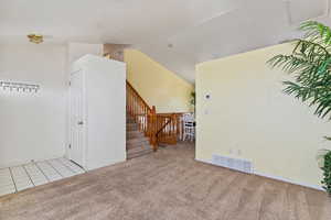Empty room with light carpet, lofted ceiling, light tile patterned floors, and stairs