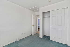 Unfurnished bedroom featuring attic access, dark colored carpet, a closet, and a textured ceiling