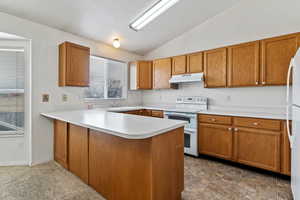 Kitchen featuring white appliances, light countertops, brown cabinetry, a peninsula, and vaulted ceiling