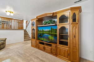 Living room featuring light colored carpet, stairway, and a textured ceiling