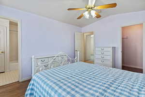 Bedroom featuring connected bathroom, dark wood-style floors, a ceiling fan, and lofted ceiling