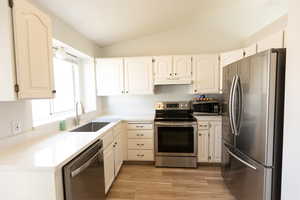 Kitchen featuring stainless steel appliances, white cabinets, lofted ceiling, light wood-style floors, and light stone countertops