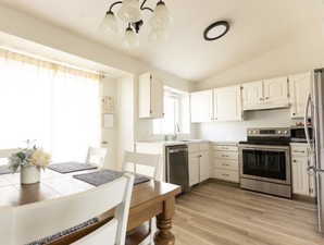 Kitchen featuring stainless steel appliances, a chandelier, white cabinetry, lofted ceiling, and light countertops
