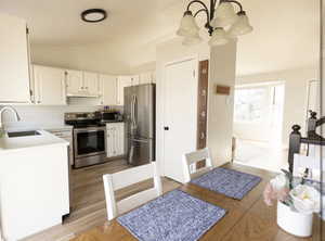 Kitchen with white cabinetry, lofted ceiling, stainless steel appliances, light wood-style floors, and hanging lights