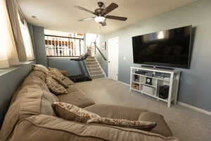 Living room with carpet floors, ceiling fan, and stairs