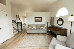 Living area featuring vaulted ceiling, light wood-style floors, and stairway