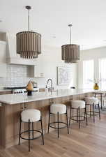 Kitchen featuring white cabinetry, light wood-style flooring, pendant lighting, and a breakfast bar area