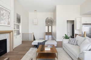 Living room with arched walkways, light wood finished floors, built in shelves, a tiled fireplace, and a high ceiling