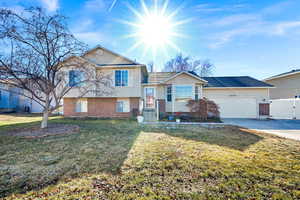 Split level home featuring brick siding, driveway, a garage, and a gate