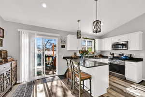 Kitchen with a peninsula, appliances with stainless steel finishes, a kitchen bar, pendant lighting, and dark wood-style flooring