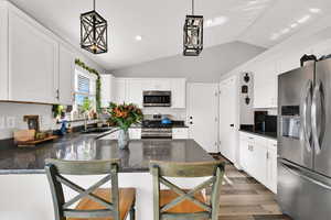 Kitchen featuring stainless steel appliances, decorative light fixtures, a peninsula, white cabinetry, and dark wood-style floors