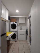 Laundry area featuring stacked washer &  clothes dryer, laundry sink and tile flooring
