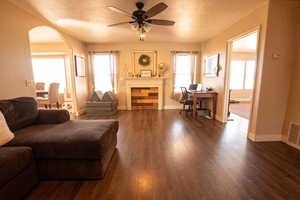Living room featuring arched walkways, dark wood-type flooring, ceiling fan, and a textured ceiling