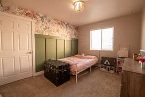 Bedroom with wallpapered walls, carpet flooring, a wainscoted wall, and a decorative wall