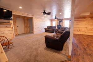 Living area with a wood stove, wood walls, a textured ceiling, a ceiling fan, and recessed lighting