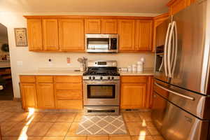 Kitchen with stainless steel appliances, brown cabinets, and light tile patterned flooring